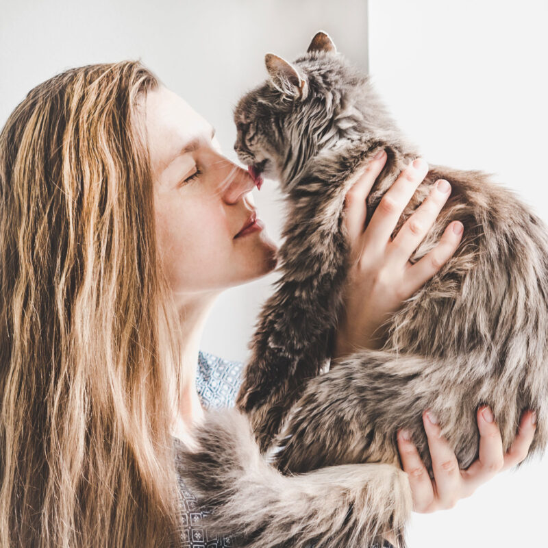 Una mujer sosteniendo a su gato cerca de su nariz y lamiéndola